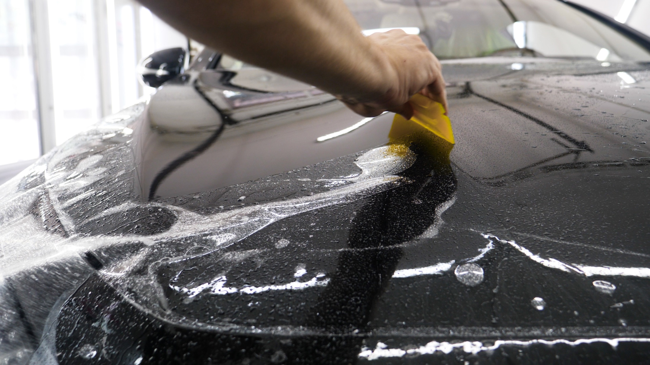 Clear paint protection film being squeegeed onto a vehicle hood